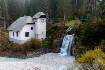 Waterfall flowing near white industrial building in misty forest