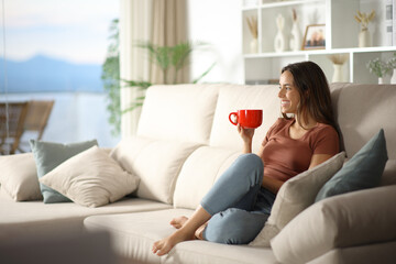 Woman in the living room at home drinking coffee from red cup