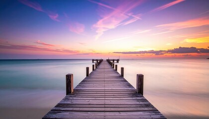 Obraz premium A serene wooden pier extends over calm waters, leading into a vibrant sunset sky filled with soft, pastel colors.
