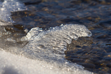 Water meeting ice shore creates captivating natural patterns in winter sunlight reflecting on...