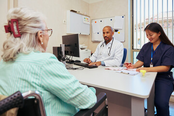 Obraz premium Doctor and nurse assisting elderly patient in wheelchair during medical consultation
