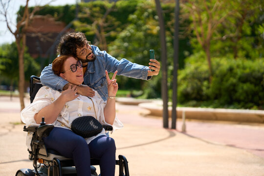 Happy diverse couple taking a selfie in the park, celebrating their love and inclusion - wheelchair and disability concept - Powered by Adobe