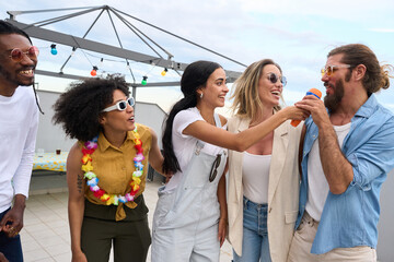 Friends singing karaoke at rooftop party, enjoying summertime together