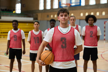 Basketball team posing on court with captain holding ball