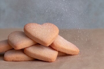 Delicate heart-shaped cookies dusted with sugar on a rustic surface