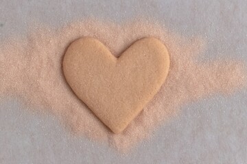 Heart-shaped cookie sitting on sandy surface during sunny afternoon baking