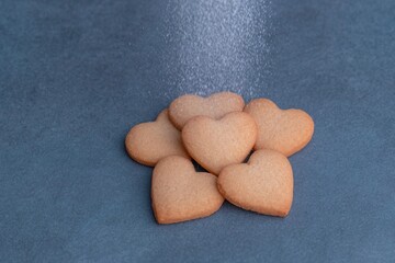 Delicate heart-shaped cookies being dusted with powdered sugar on a blue surface
