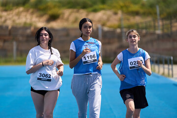 Three young female athletes running on blue track