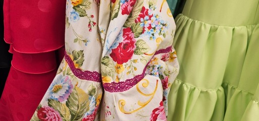 Colorful dresses on display: bright red with ruffles, floral with lace detail, and light green with...