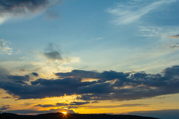 Vibrant sunset over rolling hills with dramatic clouds illuminating the evening sky and casting...