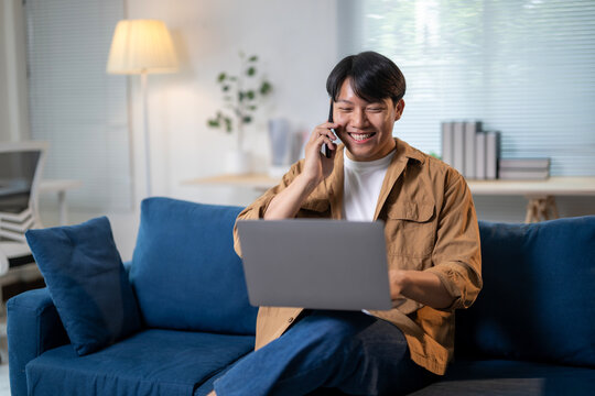 A man is sitting on a blue couch and talking on his cell phone