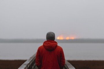 Solitary figure in a red coat gazes at distant bonfire mist, reflecting Guy Fawkes Night or Walpurgisnacht