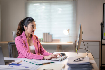 A woman in a pink jacket is typing on a computer