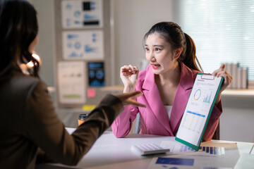 Two women are sitting at a desk with a green clipboard in front of them