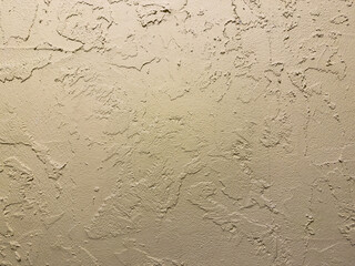 A wall with a textured surface. The wall is tan in color. The texture is rough and uneven