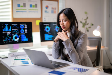 Obraz premium A woman is sitting at a desk with a laptop and a stack of papers