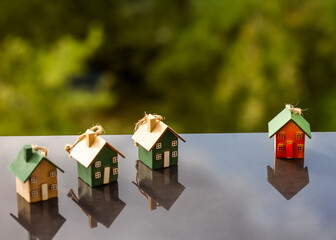 Four small wooden house ornaments on a glossy surface with green bokeh background, symbolizing home...