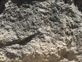 A wall made of stone. The wall is grey and has a few cracks. There are some small holes in the wall
