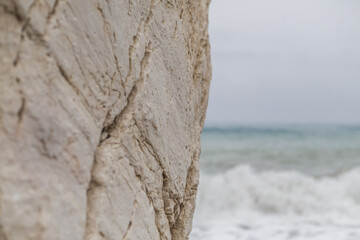 View of the rough, cream-colored rock formation contrasts with the turquoise waves crashing on the shore under a soft, overcast sky, Paphos, Paphos, Cyprus.