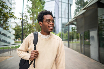 Smiling university student walking in university campus with backpack