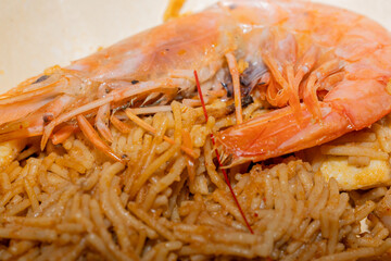 Primer plano de fideuá tradicional con gamba roja fresca sobre fideos. / Close-up of traditional fideuá with fresh red prawn on noodles.