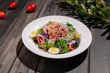 Fresh salad with tuna, eggs, and vegetables on wooden table