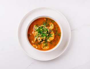 Spicy seafood soup with fresh herbs in a deep white bowl