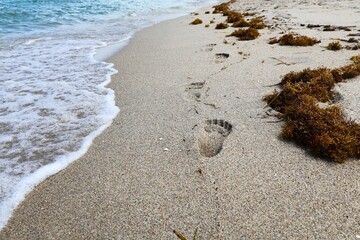 Chain of footprint in the sand with waves rolling on beach