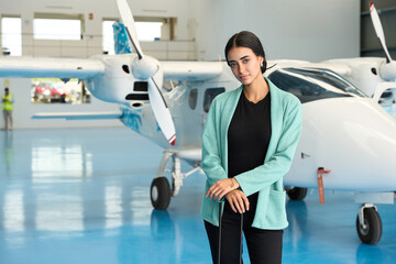 Confident aircraft maintenance engineer posing in hangar with small airplane