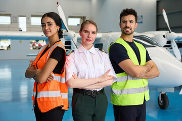Pilot and aircraft mechanics posing with arms crossed in hangar
