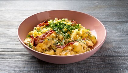 Potato sald with fresh herbs , scrambled eggs and bacon in a pale pink ceramic bowl on gray wooden table. Generated image