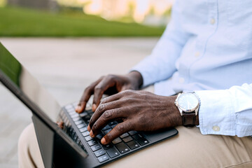 Businessman in professional attire types on laptop in outdoor setting during a sunny day