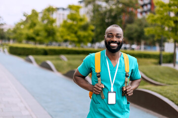Smiling male nurse walking in the park wearing scrubs and carrying a backpack during daytime
