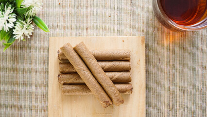 Top view of delicious chocolate wafer roll on a wooden board with a cup of tea isolated on wooden...