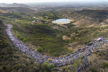 Aerial view of a massive crowd gathered in a valley near a water reservoir, bordered by lush greenery and distant hills, Pandharpur, Maharashtra, India.