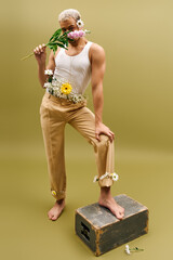 Young man in trendy tank top adorned with flowers poses stylishly in studio setting