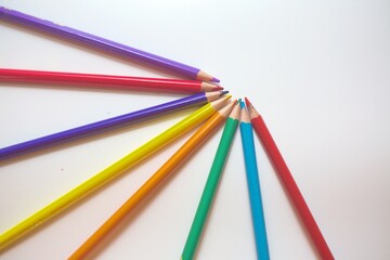 Fototapeta premium Colored Pencils Arranged in a Fan Pattern on White. An artistic arrangement of sharpened colored pencils fanned out in a semi-circle against a white surface.