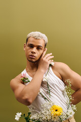 Young Black man in a stylish tank top surrounded by flowers in a studio