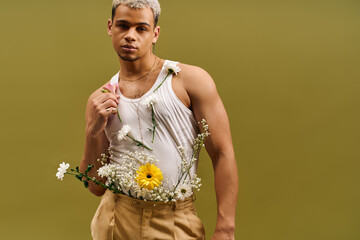Stylish young man in tank top poses with flowers in vibrant studio setting