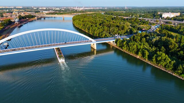 Riverboat goes slowly under the gorgeous Appolo Bridge. Drone footage over the Danube River in Bratislava, Slovakia on a beautiful summer day.
