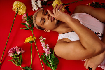 Young man showcases trendy fashion with vibrant floral arrangement in a red studio