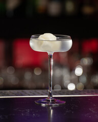 A light-colored alcoholic cocktail with a scoop of white sorbet or ice cream is presented in a...