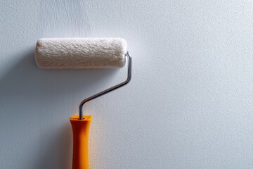 Obraz premium Orange handle paint roller on white wall surface: diy home improvement