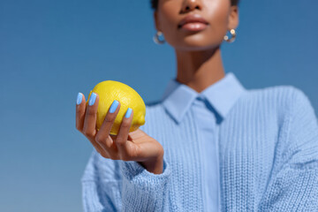 Woman holding lemon with matching manicure under blue sky