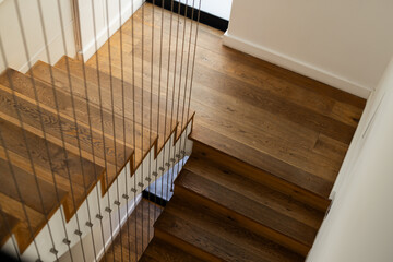 L-shaped wooden staircase is showing cable railing and hardwood treads against white walls