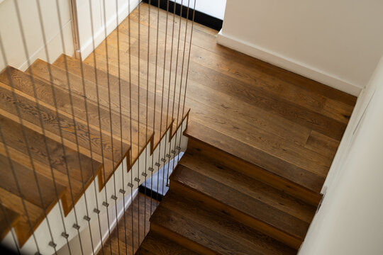 L-shaped wooden staircase is showing cable railing and hardwood treads against white walls