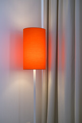 Minimalist red-orange standing lamp casting warm glow on curtain and wall, creating a cozy ambiance...