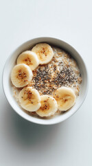 A bowl of oatmeal topped with sliced bananas and chia seeds. The dish is placed on a white surface, emphasizing a healthy breakfast concept.