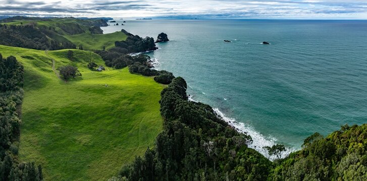 Aerial view of the lush green hills and coastline of Whiritoa, New Zealand. The landscape shows the beauty of nature, with rolling hills meeting the turquoise ocean.