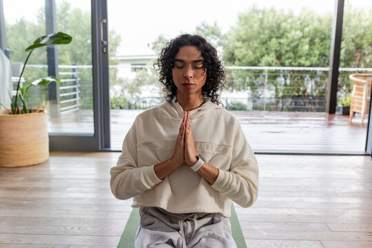 Non-binary person sitting cross-legged on green yoga mat at home, holding smartwatch and meditating